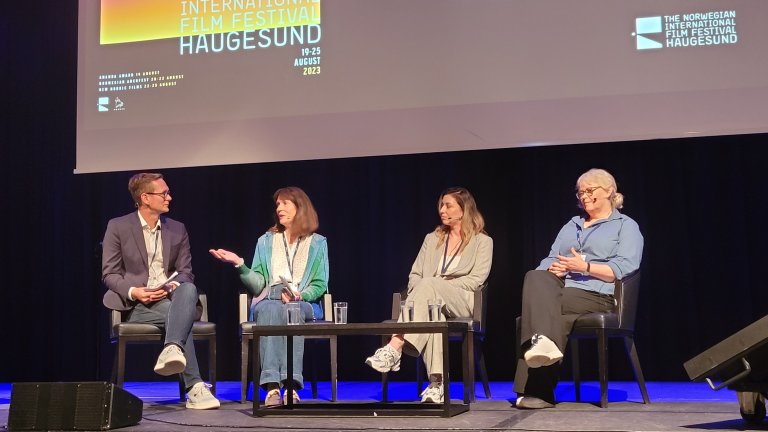 Fire personer sitter på en scene, en mann til venstre og tre kvinner foran en storskjerm med logoen til filmfestivalen i Haugesund