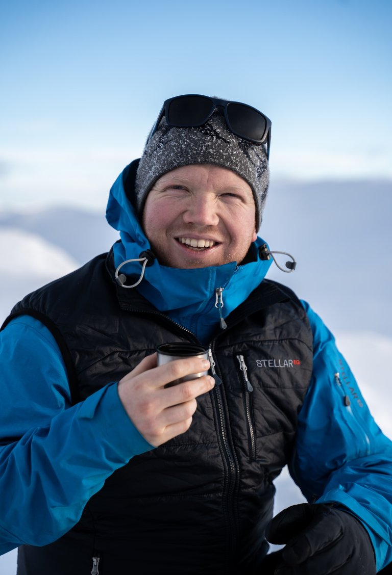 foto. mann med overlevelsesdrakt og solbriller sitter ute i snølandskap