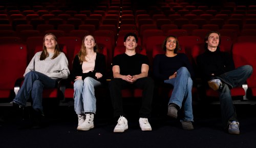 foto. fem unge mennesker sitter på rad i en kinosal med røde seter