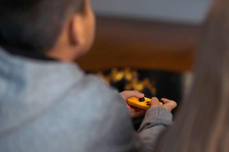 Bilde. Et barn i grå hettegenser holder en gul spillkontroll.